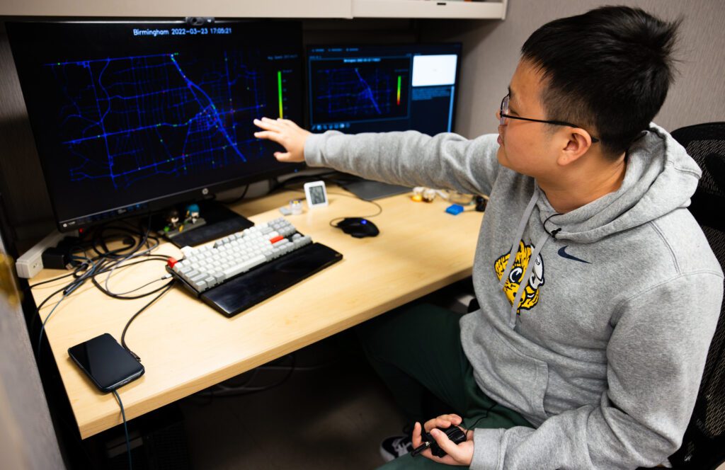 Xingmin Wang stands in front of a computer that is visualizing vehicle trajectory data