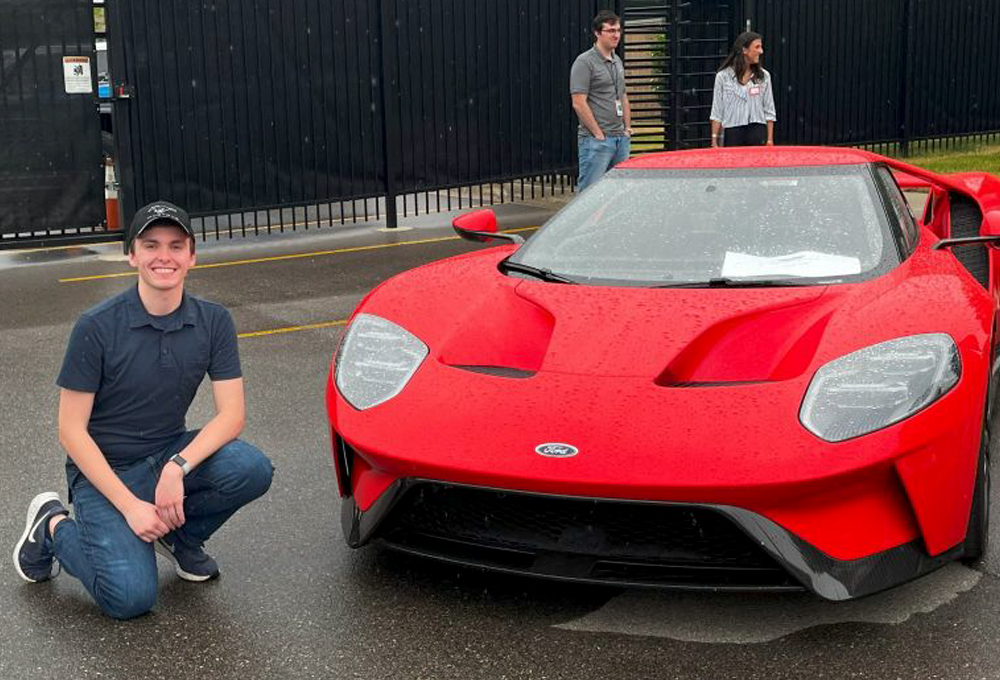 Young white man crouches next to a red sportscar