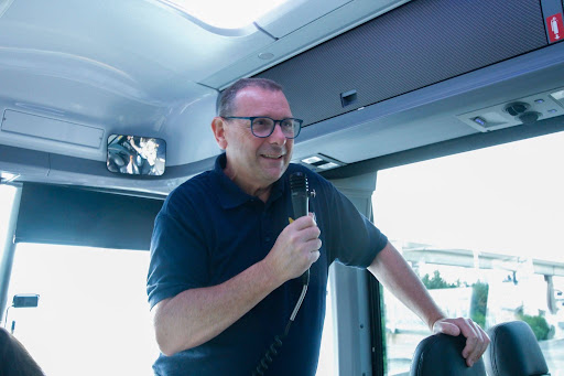 Andrew Donaldson at the front of a bus with a microphone in their hand